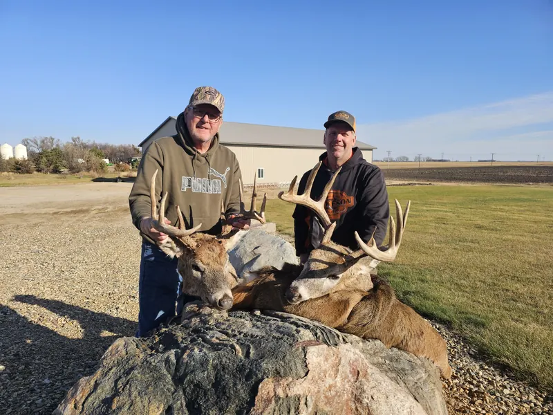 Two hunters with two whitetail bucks on a rock outside the farm shop