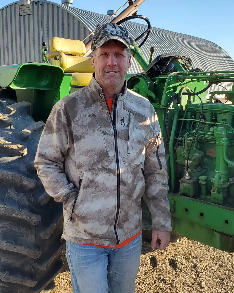 Carl Hanson standing in front of a John Deere tractor on the farm